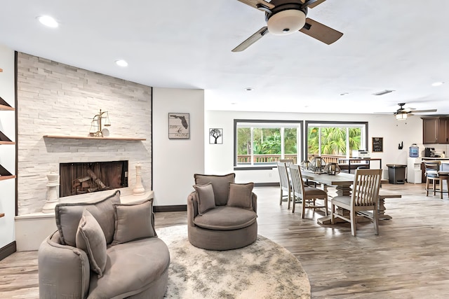 living room with ceiling fan, a large fireplace, and light hardwood / wood-style floors