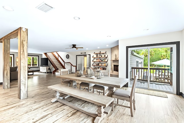 dining space with a large fireplace, a wealth of natural light, ceiling fan, and light hardwood / wood-style flooring