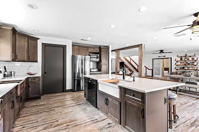 kitchen featuring black dishwasher, sink, a kitchen island with sink, stainless steel refrigerator, and light wood-type flooring