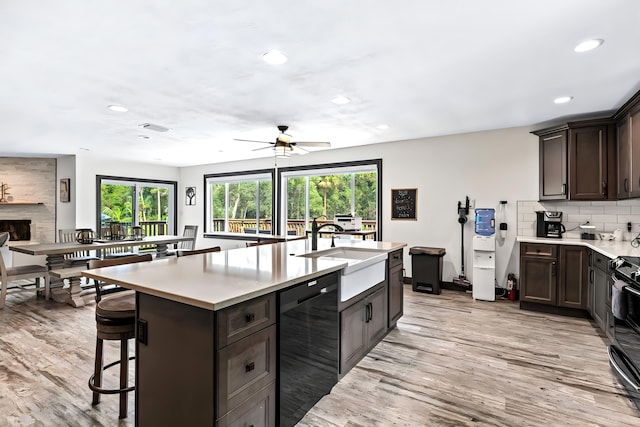 kitchen with light hardwood / wood-style flooring, sink, a large fireplace, a breakfast bar area, and a kitchen island with sink