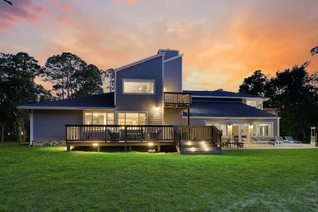 back house at dusk featuring a lawn, a deck, and a patio area