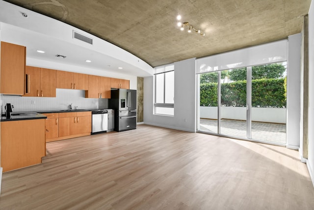 kitchen with a sink, dark countertops, backsplash, stainless steel appliances, and light wood-style floors