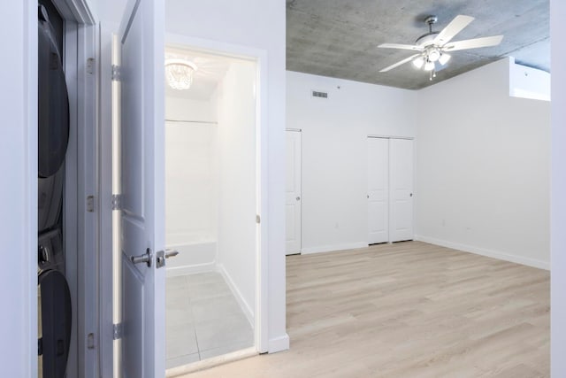 empty room with light hardwood / wood-style flooring, ceiling fan, and stacked washer / drying machine