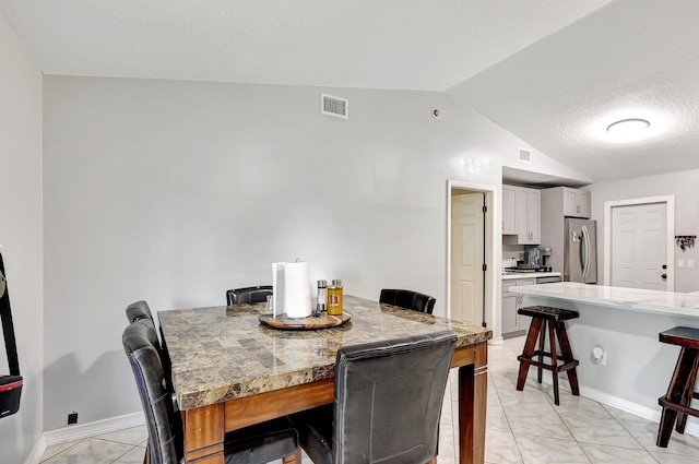 dining space featuring lofted ceiling, a textured ceiling, and light tile patterned floors