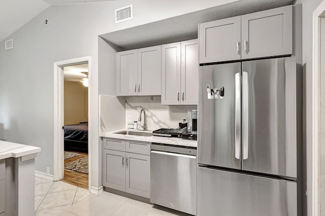 kitchen with light tile patterned flooring, stainless steel appliances, gray cabinets, sink, and vaulted ceiling