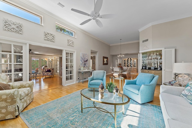 living room featuring ornamental molding, light hardwood / wood-style floors, french doors, ceiling fan with notable chandelier, and a towering ceiling