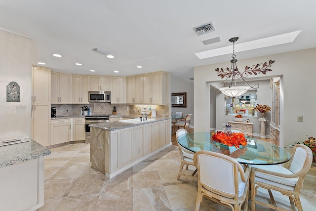 kitchen featuring tasteful backsplash, light stone counters, stainless steel appliances, decorative light fixtures, and cream cabinetry