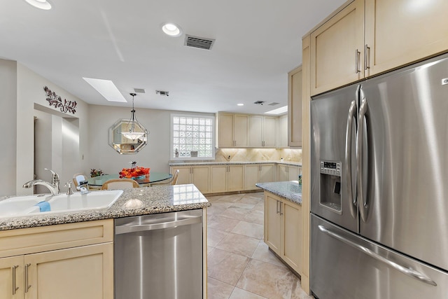 kitchen with a skylight, stainless steel appliances, sink, cream cabinets, and light tile patterned floors