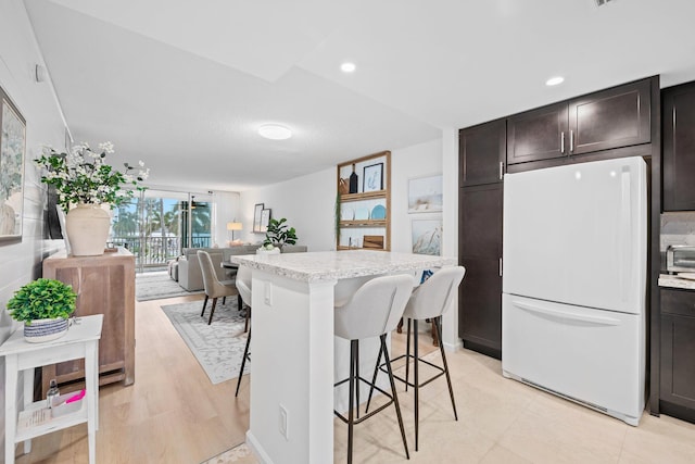 kitchen featuring white fridge, a center island, dark brown cabinets, a breakfast bar area, and light hardwood / wood-style flooring