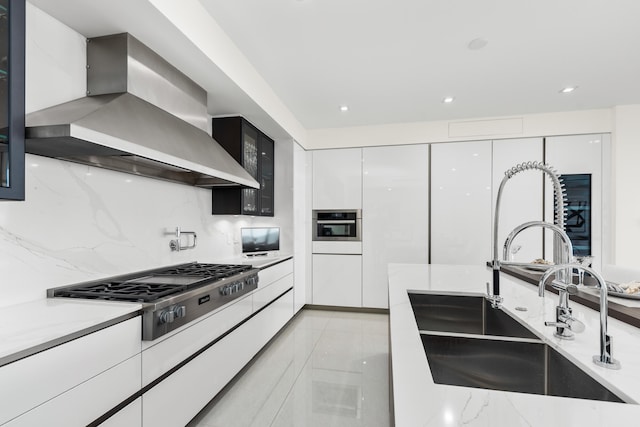 kitchen with stainless steel appliances, white cabinetry, sink, wall chimney range hood, and decorative backsplash