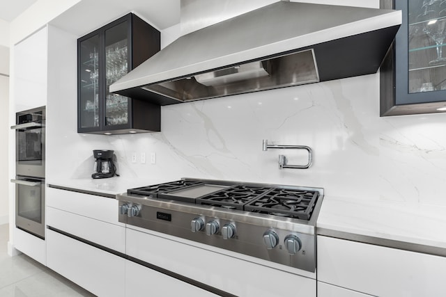 kitchen with appliances with stainless steel finishes, light stone countertops, decorative backsplash, white cabinets, and wall chimney exhaust hood