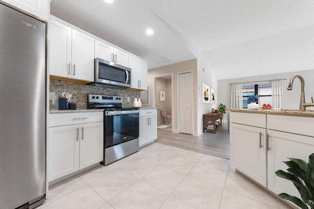 kitchen with white cabinets, a textured ceiling, vaulted ceiling, and stainless steel appliances