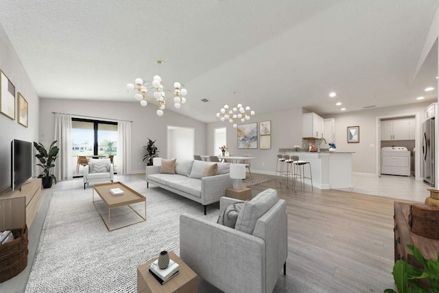 living room with a textured ceiling, washer / clothes dryer, vaulted ceiling, light hardwood / wood-style floors, and a chandelier