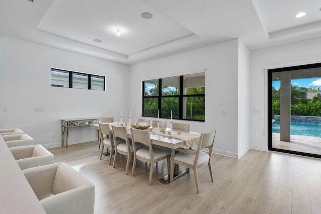 dining room featuring a healthy amount of sunlight, light wood finished floors, and a raised ceiling