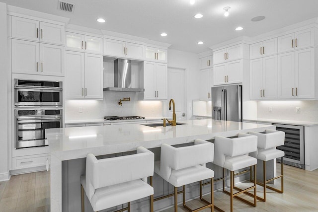 kitchen with beverage cooler, visible vents, wall chimney exhaust hood, stainless steel appliances, and a sink