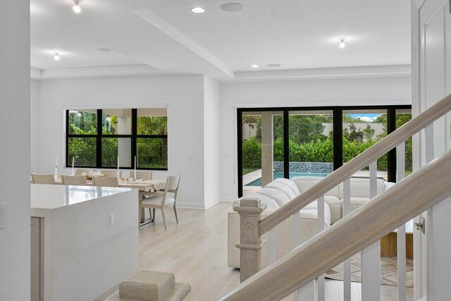 kitchen with light wood-type flooring, a raised ceiling, sink, an island with sink, and stainless steel dishwasher