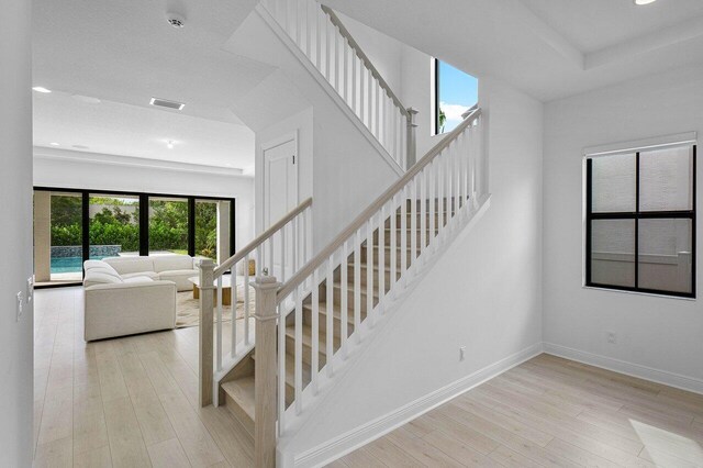 hallway with light wood-type flooring, a tray ceiling, baseboards, and stairs