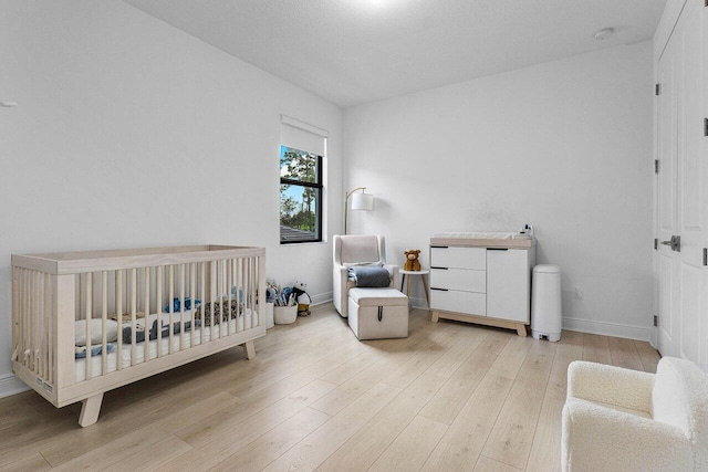 bedroom with a nursery area, baseboards, and light wood-style floors