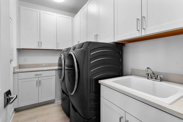 clothes washing area with a sink, light wood-style flooring, washing machine and clothes dryer, and cabinet space