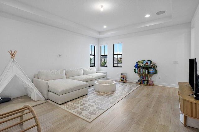 living area with baseboards, recessed lighting, a raised ceiling, and light wood-style floors