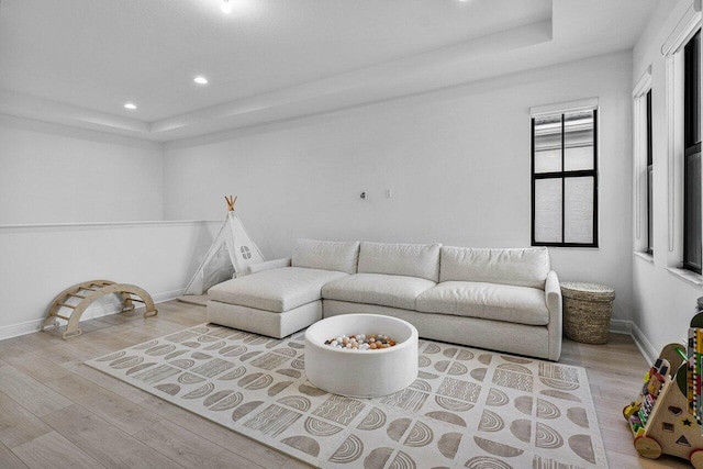 living area featuring a tray ceiling, recessed lighting, wood finished floors, and baseboards