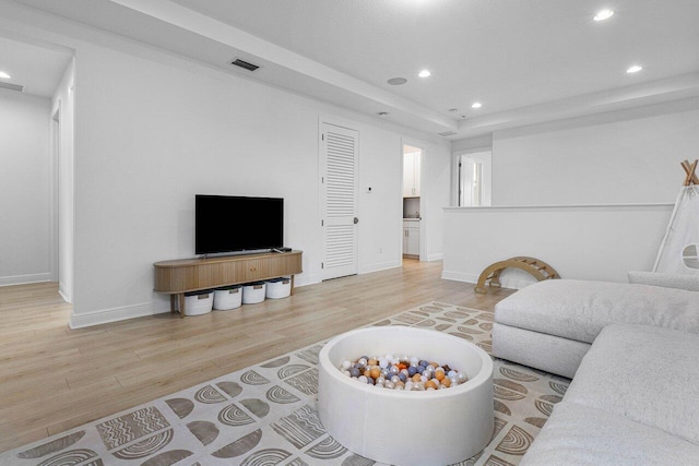 living area with recessed lighting, wood finished floors, visible vents, baseboards, and a raised ceiling