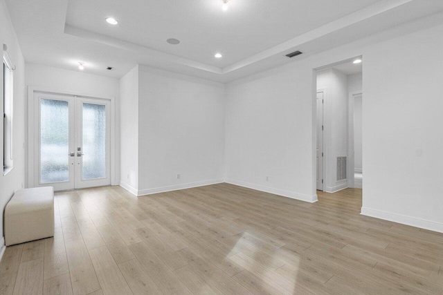 unfurnished room with light wood-style floors, visible vents, a raised ceiling, and french doors