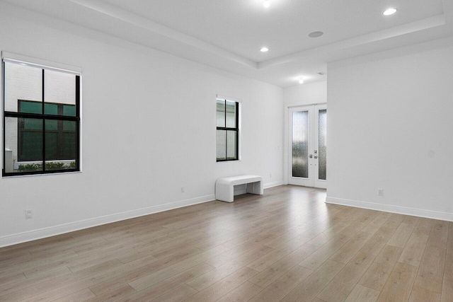 spare room featuring a healthy amount of sunlight, a raised ceiling, light hardwood / wood-style flooring, and french doors