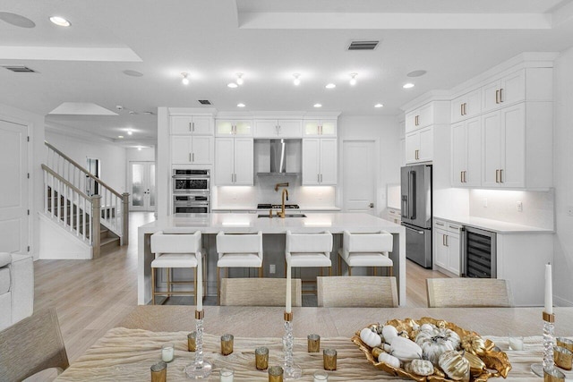 kitchen with stainless steel appliances, wine cooler, tasteful backsplash, a breakfast bar area, and wall chimney range hood