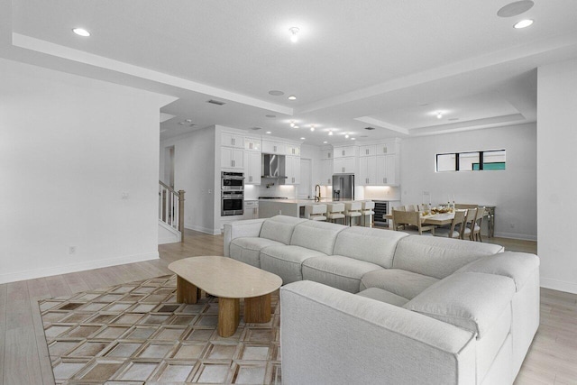 living room with light wood-type flooring and a tray ceiling