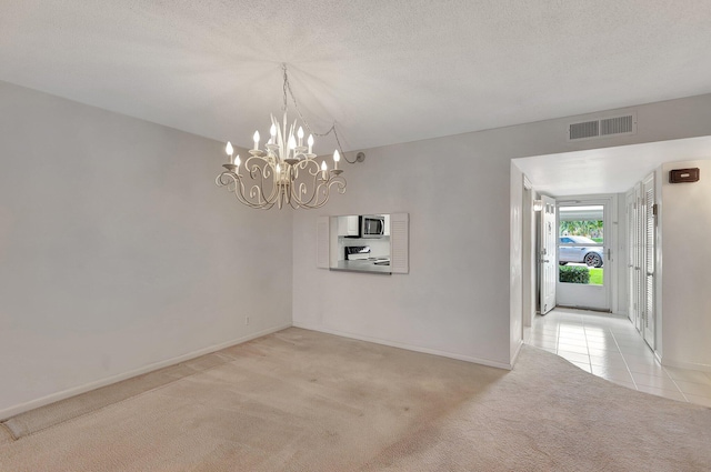 carpeted empty room with a textured ceiling and an inviting chandelier