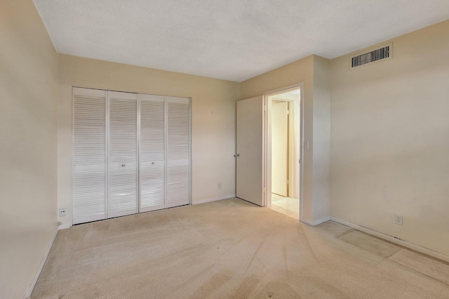 unfurnished bedroom featuring light colored carpet, a textured ceiling, and a closet