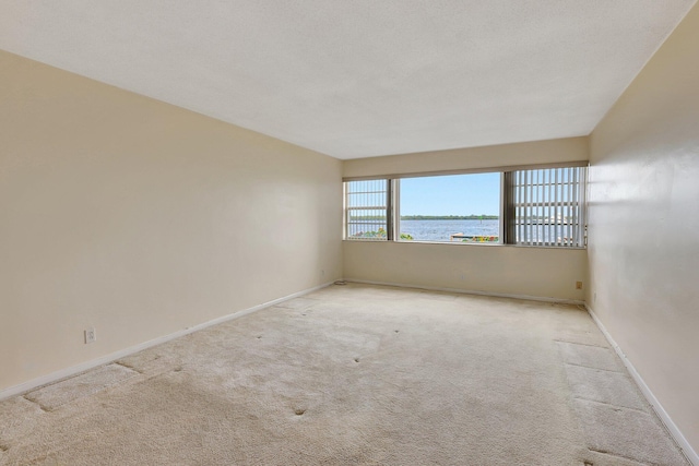 empty room with a water view, a textured ceiling, and light carpet