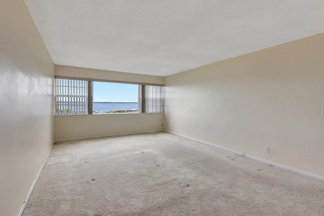 carpeted empty room with a water view and a textured ceiling