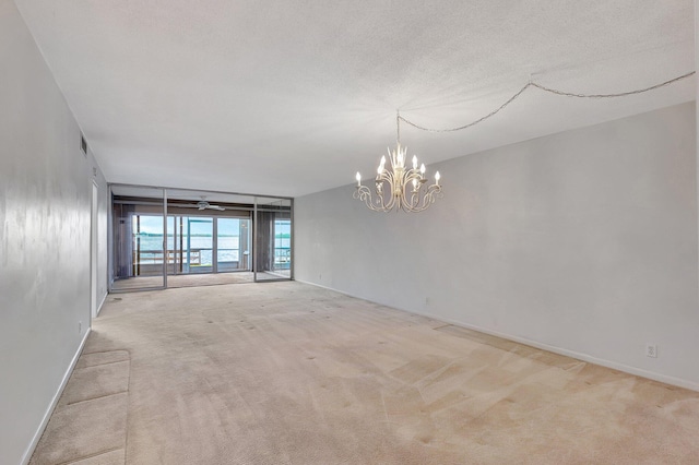 empty room with a textured ceiling, a notable chandelier, and light carpet