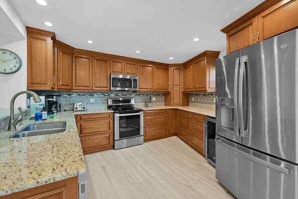 kitchen with light stone countertops, appliances with stainless steel finishes, sink, and light hardwood / wood-style flooring