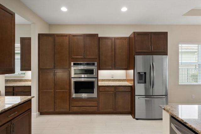 kitchen with light stone countertops, appliances with stainless steel finishes, and dark brown cabinets