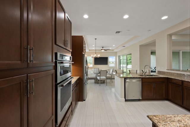 kitchen with stainless steel appliances, a raised ceiling, sink, and light stone counters