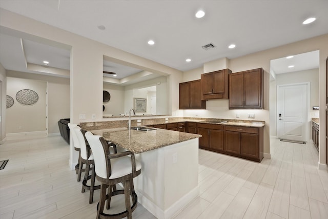 kitchen with a kitchen bar, sink, kitchen peninsula, black electric stovetop, and light stone countertops