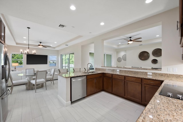 kitchen with sink, light stone counters, appliances with stainless steel finishes, a raised ceiling, and kitchen peninsula