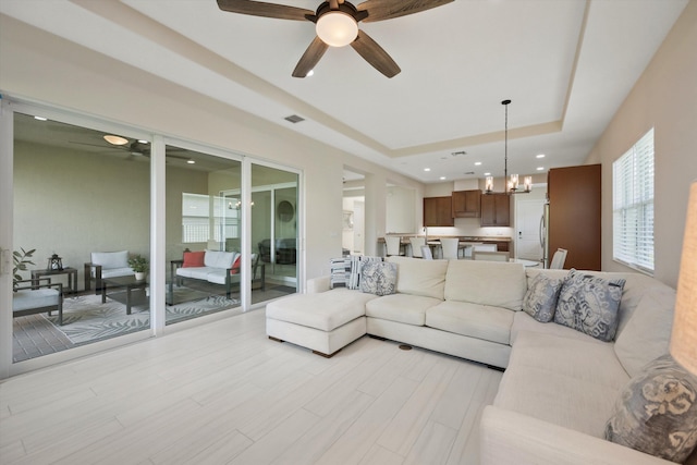 living room featuring a tray ceiling, ceiling fan with notable chandelier, and light wood-type flooring