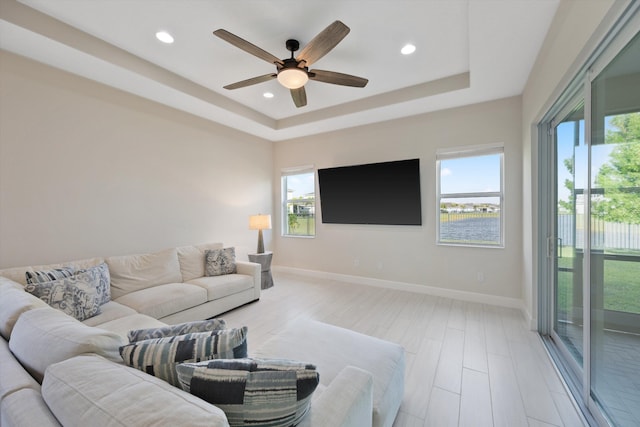 living room featuring ceiling fan, plenty of natural light, a raised ceiling, and light hardwood / wood-style floors