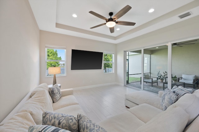 living room featuring plenty of natural light, a raised ceiling, and light wood-type flooring