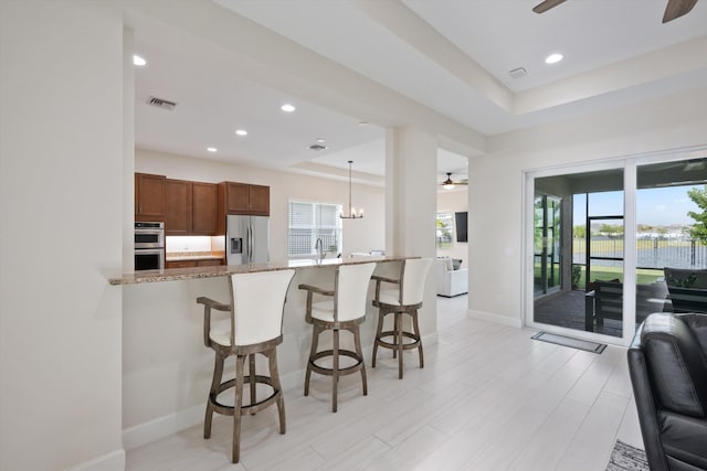 kitchen featuring ceiling fan, stone counters, appliances with stainless steel finishes, decorative light fixtures, and a raised ceiling