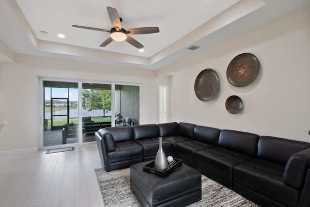 living room with a tray ceiling, light hardwood / wood-style floors, and ceiling fan