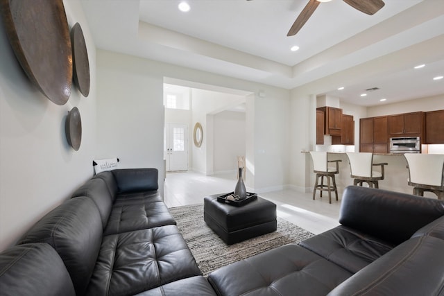 living room with light hardwood / wood-style flooring, a raised ceiling, and ceiling fan