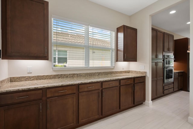 kitchen featuring light stone countertops, double oven, and dark brown cabinets