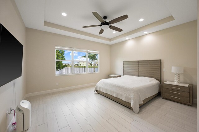 bedroom featuring ceiling fan, light hardwood / wood-style floors, and a tray ceiling