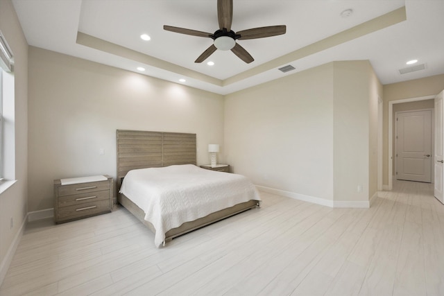 bedroom with light hardwood / wood-style floors, a raised ceiling, and ceiling fan