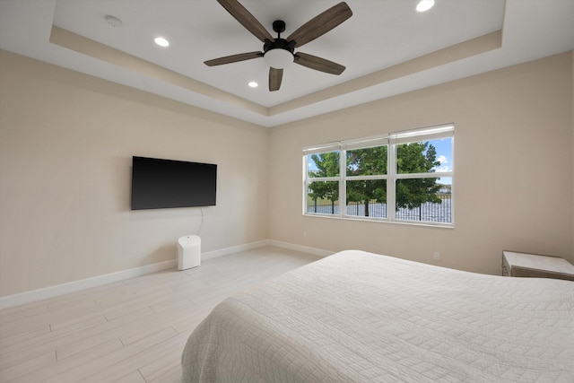 bedroom with a tray ceiling, light hardwood / wood-style floors, and ceiling fan